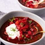 2 bowls of borscht topped with sour cream and fresh dill