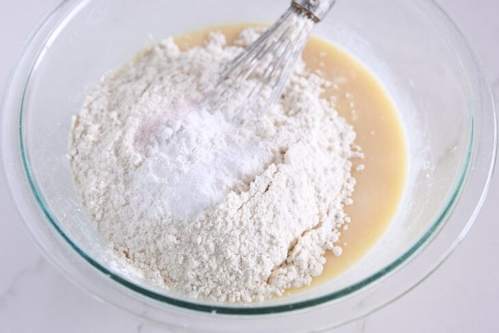 Flour, baking soda, baking powder and salt on top of quick bread batter in glass bowl.