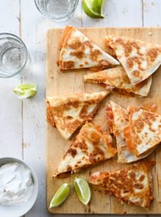 chicken quesadillas on wooden cutting board with limes and sour cream
