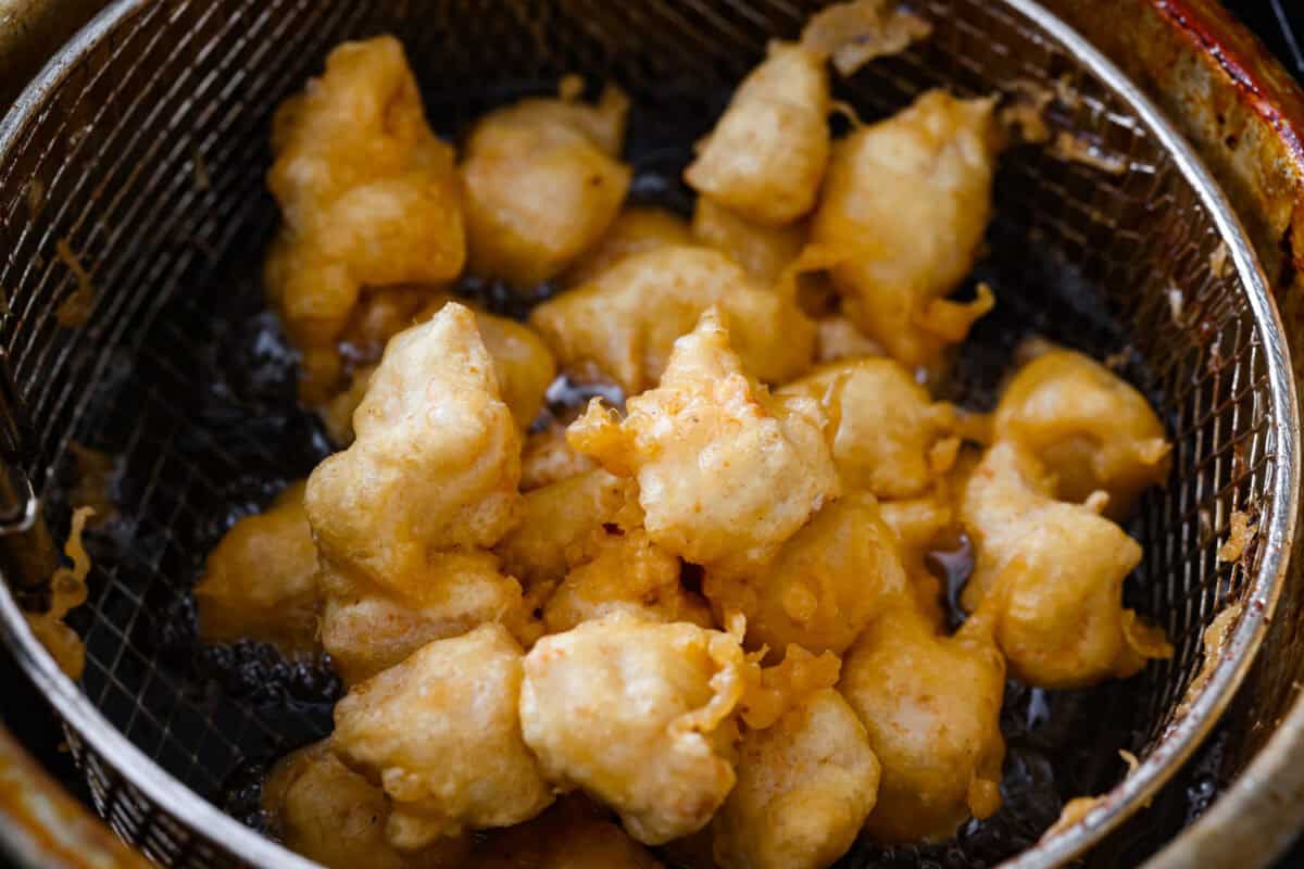 Chicken pieces frying in a deep fryer basket.