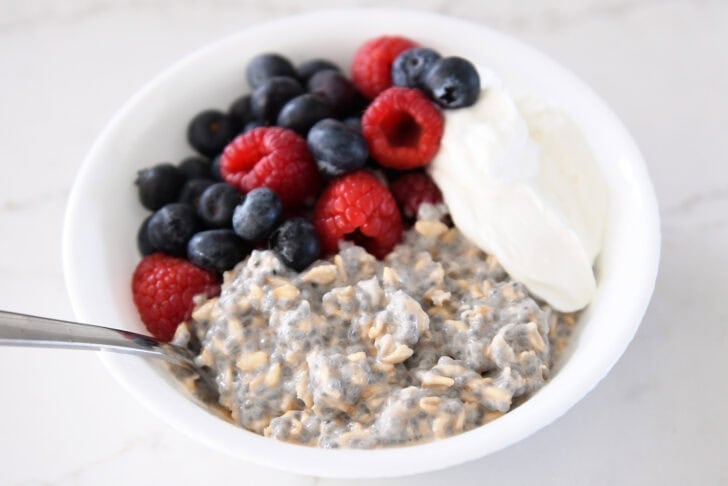 White bowl with chia oats, blueberries, Greek yogurt, and raspberries.