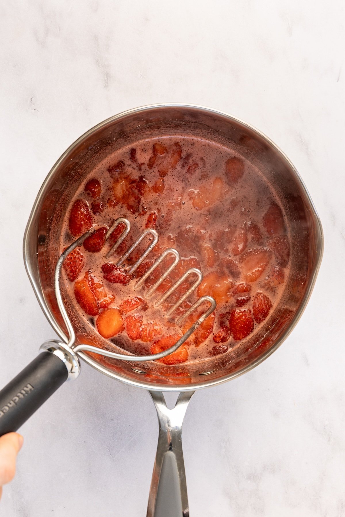 mashing berries with potato masher in medium pot