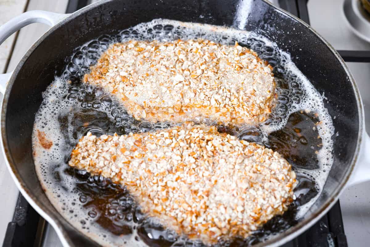 Pretzel crusted chicken coated and frying in a skillet. 