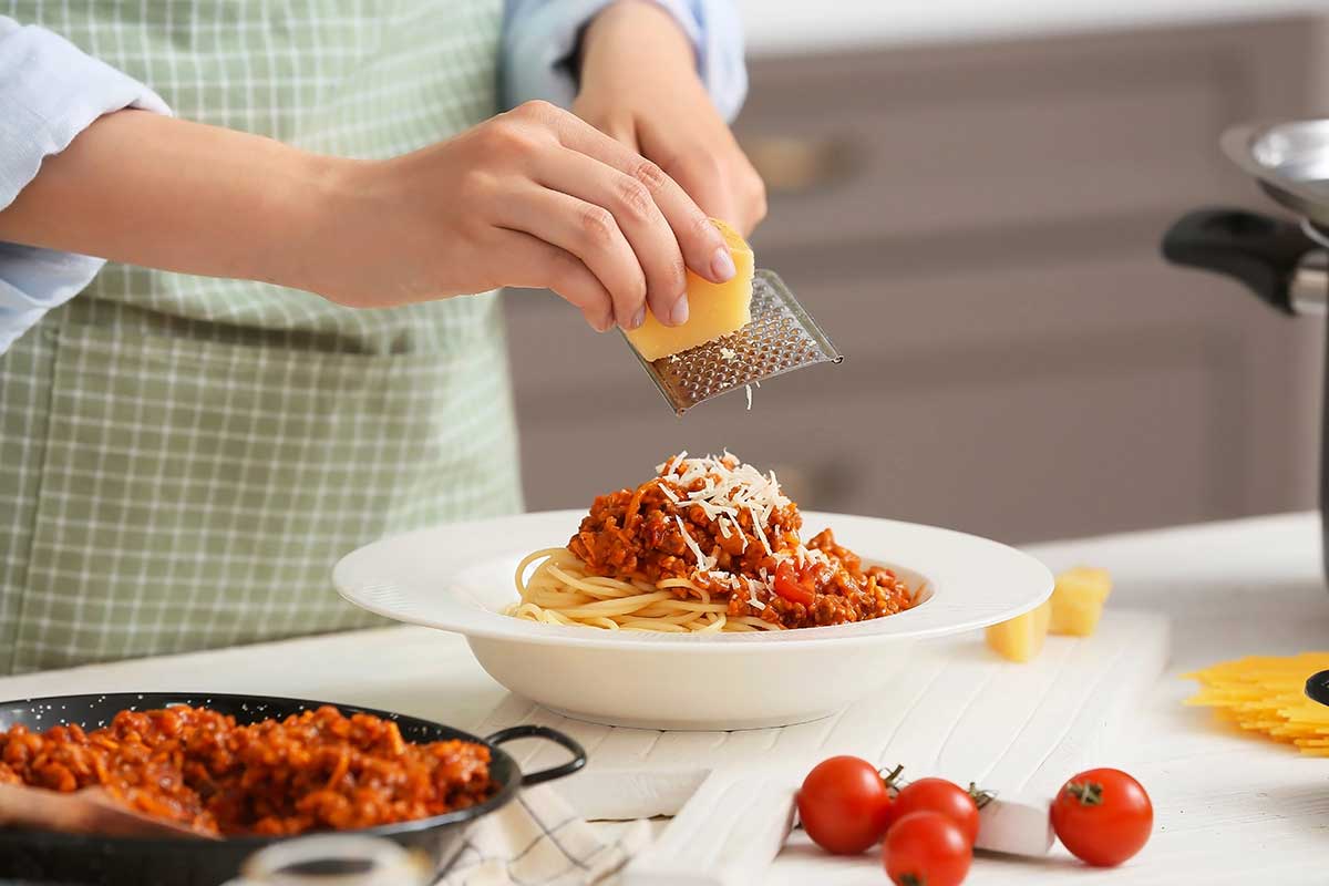 Freshly grated Parmesan being grated over a bowl of marinara pasta