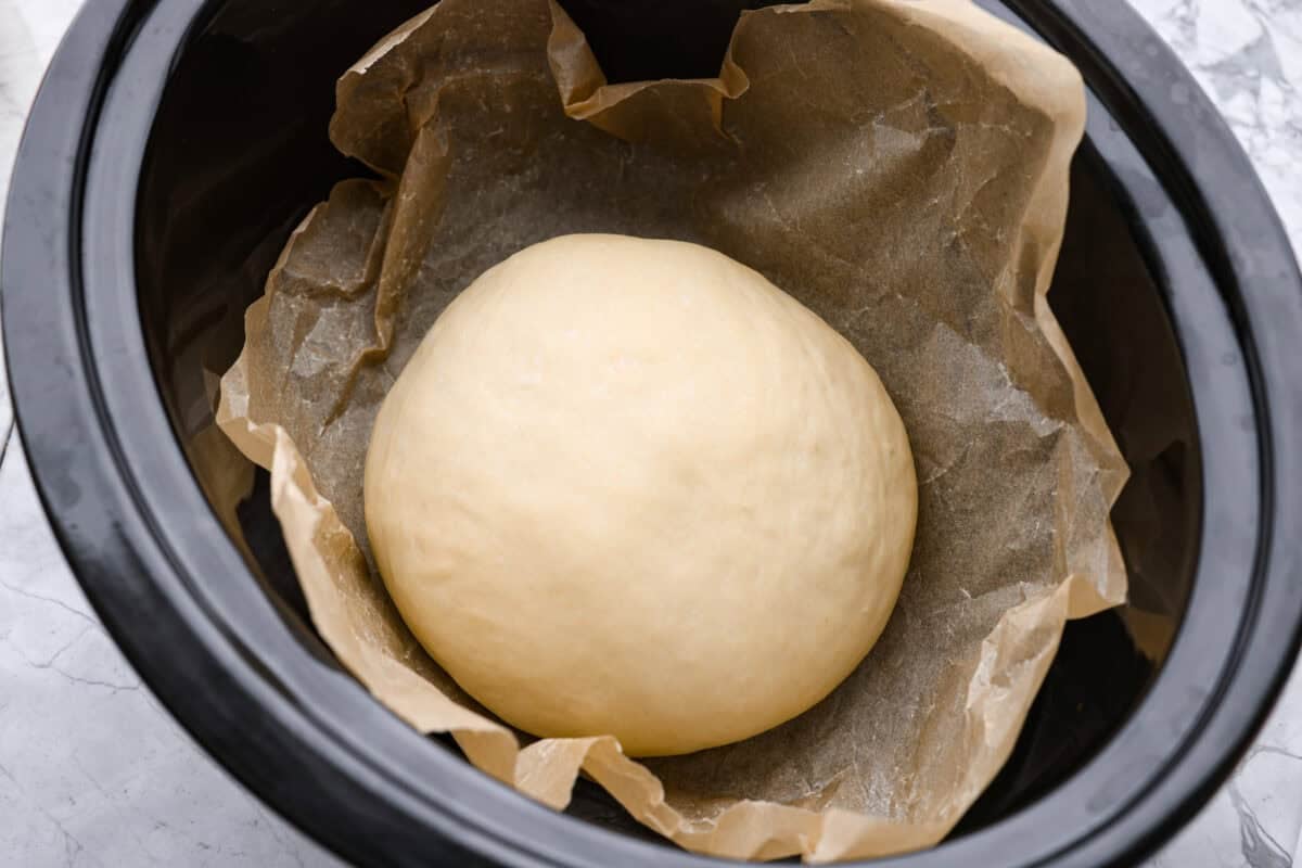 Ball of dough added to the crockpot on top of a piece of parchment paper. 