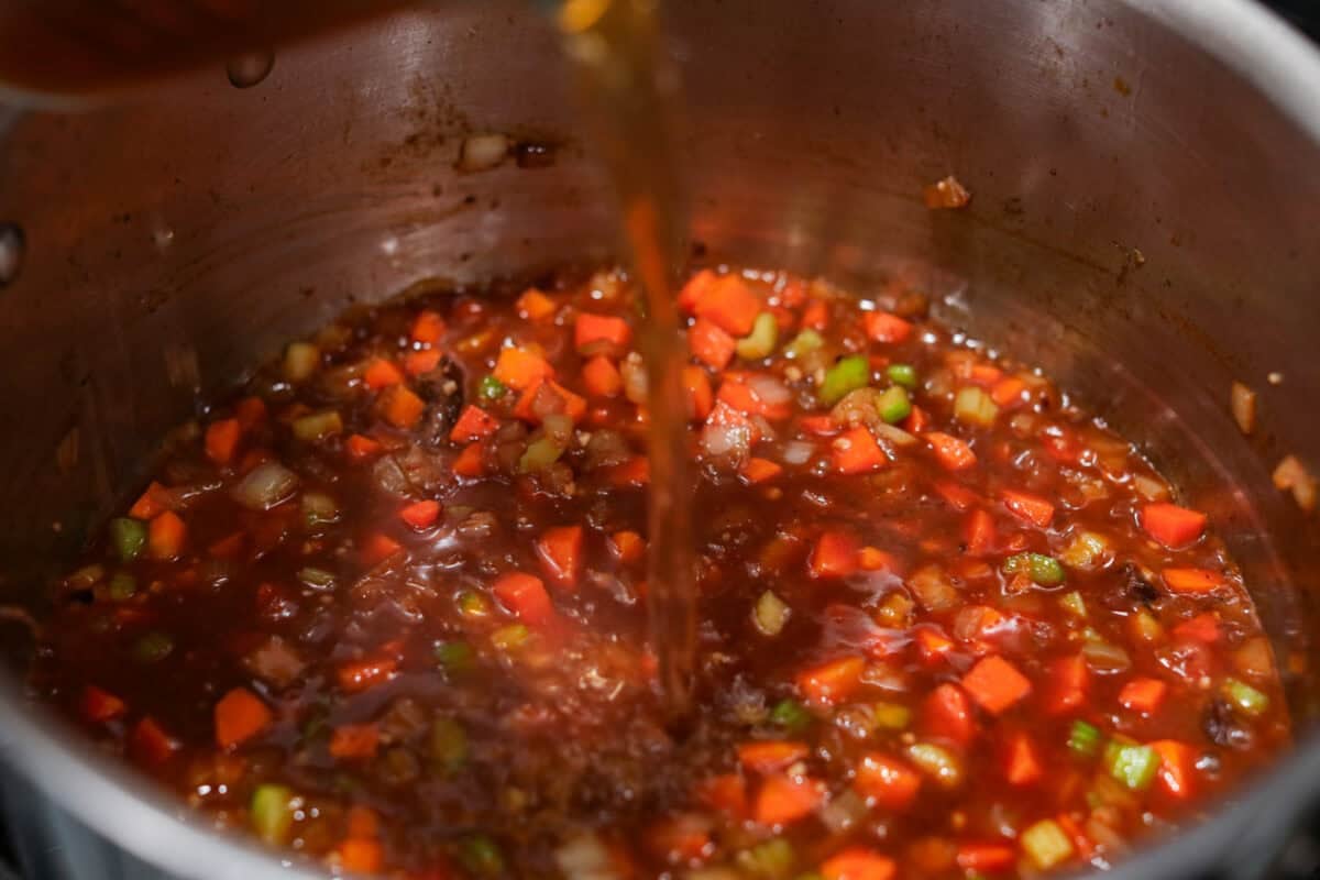 Beef broth being added to the veggie and wine mixture. 