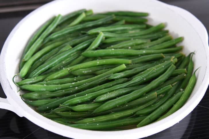 White skillet with broth, cooked green beans and salt.