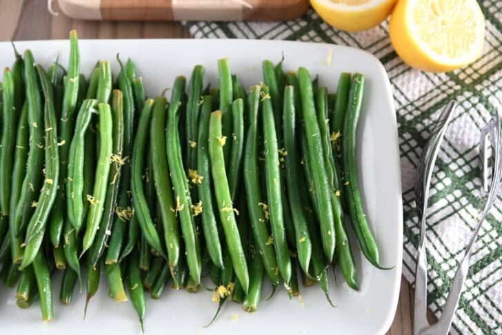 White tray with cooked green beans and lemon zest.