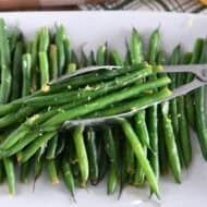 White tray with cooked green beans, lemon zest and tons scooping up portion of green beans.