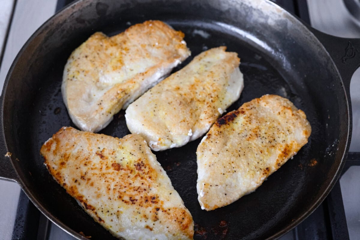 Chicken breasts cooking in a skillet.