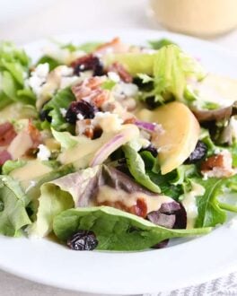 dished up portion of spinach salad on white plate with vinaigrette, bacon, onions and feta