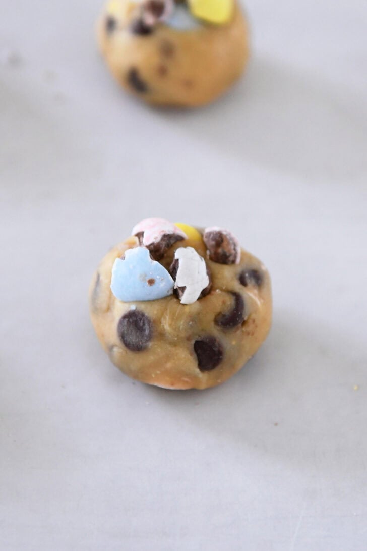 Cookie dough ball topped with crushed cadbury eggs on parchment lined baking sheet.
