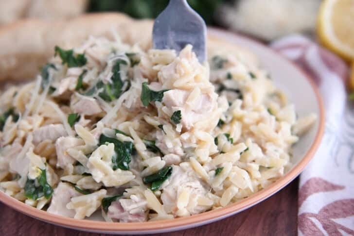 Creamy orzo with spinach and chicken on white plate with fork.