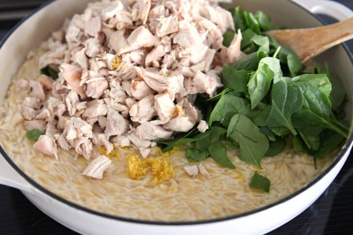 Chopped chicken, lemon zest and fresh spinach in white pan with creamy orzo.