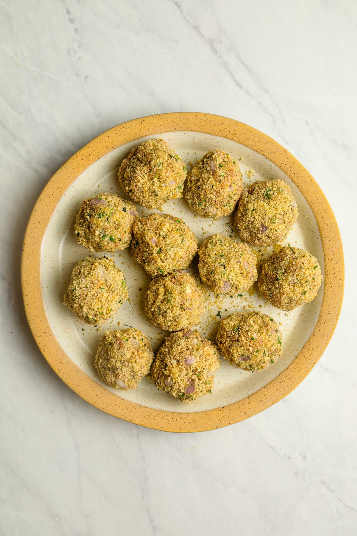 plate with 12 uncooked chicken meatballs coated with breadcrumbs