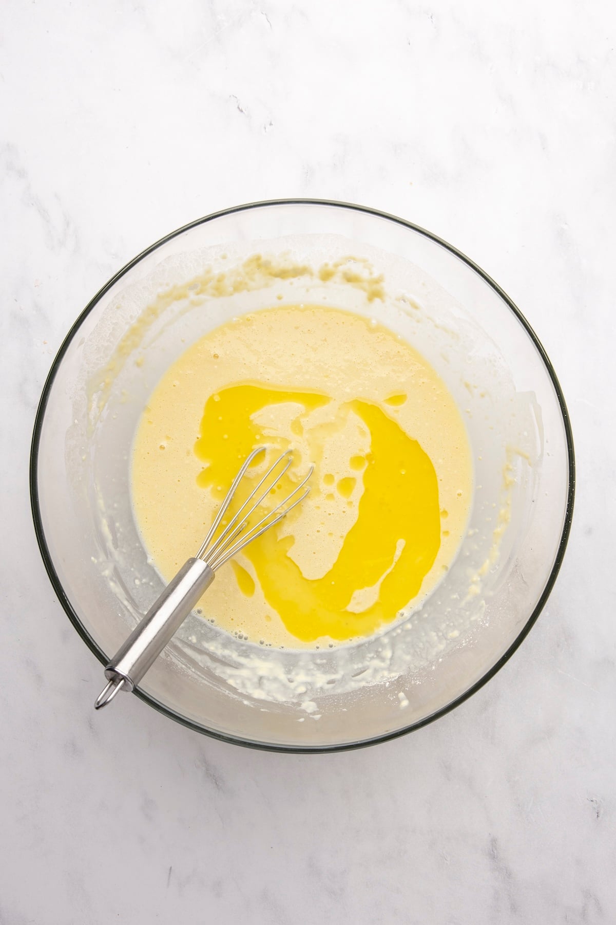 adding melted butter to large bowl with milk, egg, and flour mixture