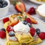 white plate with 3 cheese blintzes topped with sour cream, confectioners' sugar, and fresh berries