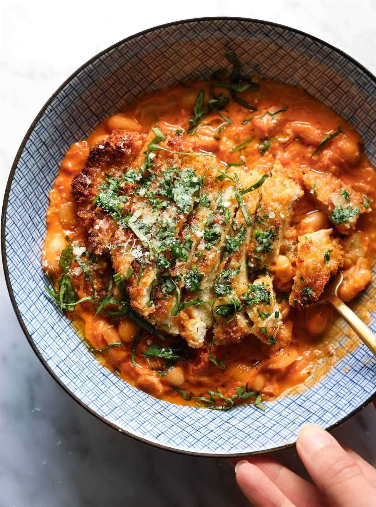 Crispy chicken with creamy beans in a blue bowl topped with basil