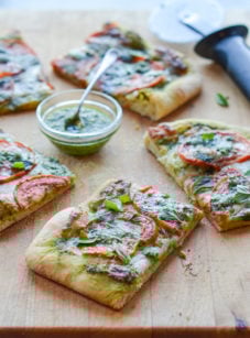 Slices of pesto pizza with fresh tomatoes and mozzarella on a wooden board.