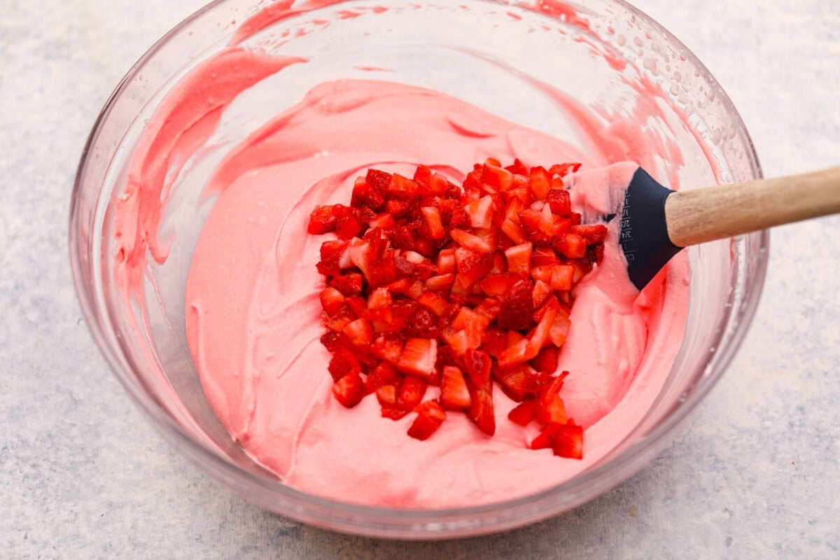 Gelatin, whipped cream, and strawberries all added to a bowl. 