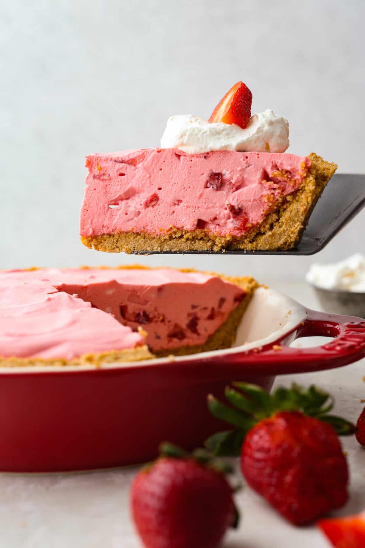 Someone lifting a slice of no bake strawberry cream pie from the pie pan. 