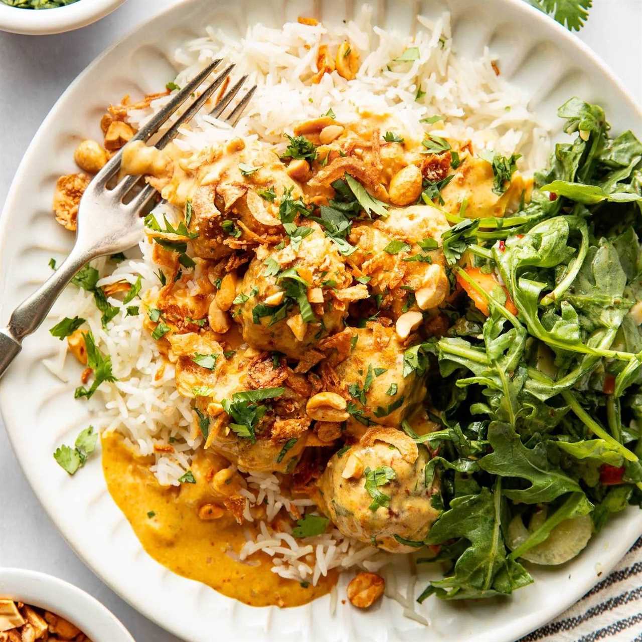 Yellow curry meatballs on a plate with rice and greens.