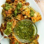 Grilled chimichurri chicken thighs on platter with chimichurri sauce.