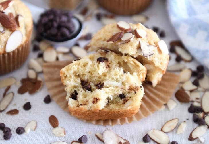 One almond coconut chocolate chip muffin broken in half on brown paper liner.
