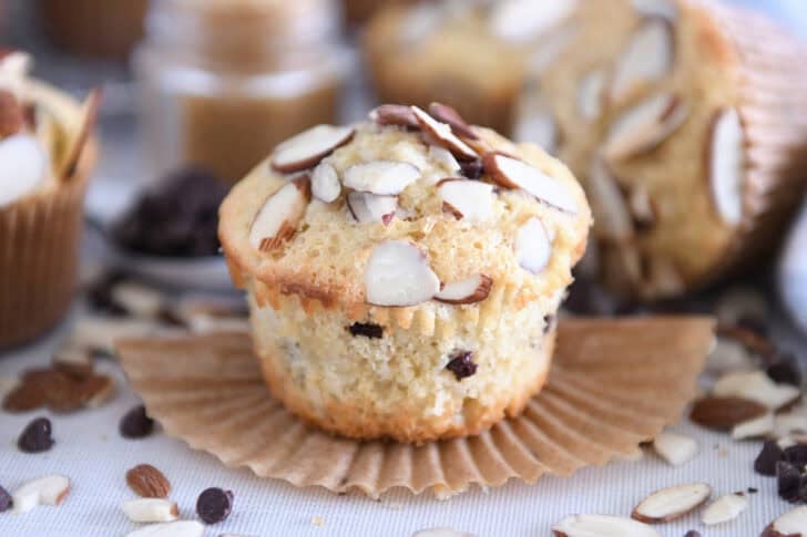 Unwrapped almond coconut chocolate chip muffin on brown paper muffin liner.