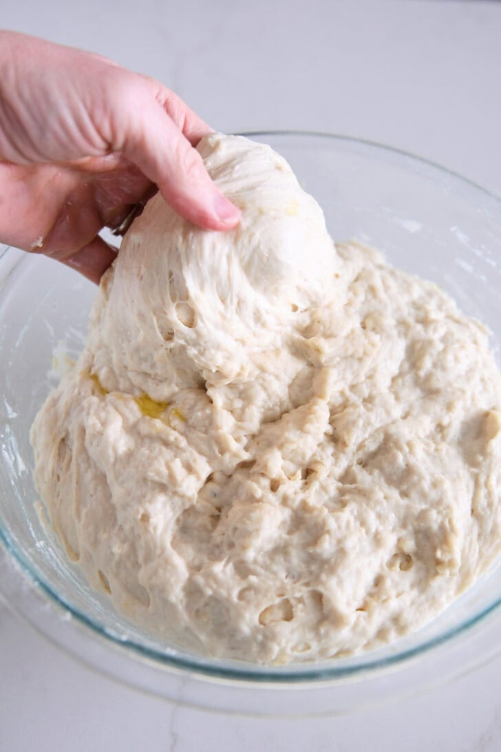 Stretching and folding focaccia dough in glass bowl.