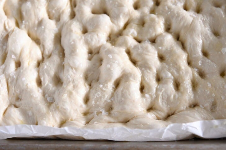 Unbaked focaccia dough in parchment lined 9X13-inch pan.