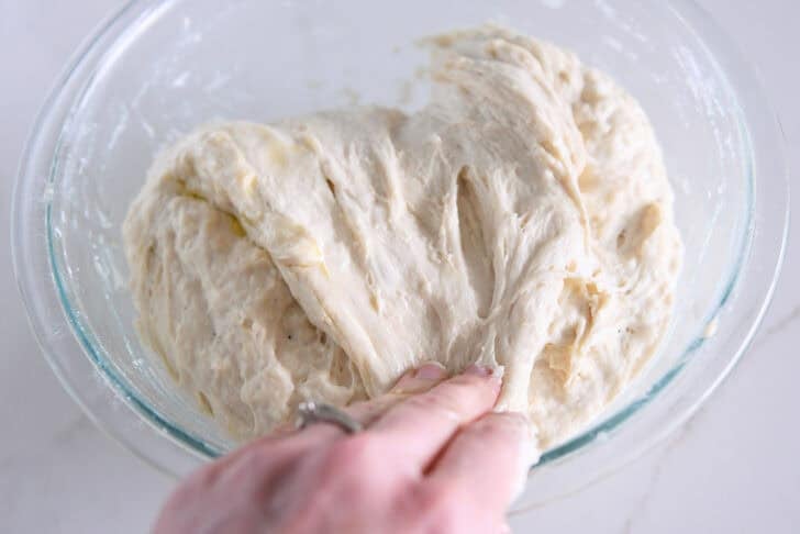Stretching and folding focaccia dough in glass bowl.