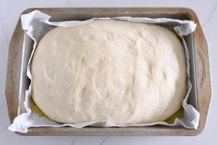 Risen unbaked focaccia bread in parchment lined 9X13-inch baking pan.