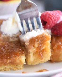 A fork taking a bite out of a caramelized french toast bake on a white plate.