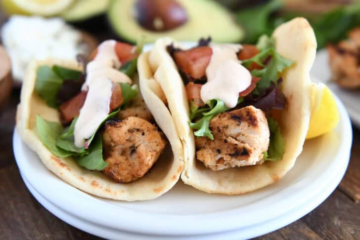 Flatbread grilled chicken wraps with lettuce, tomatoes, and creamy sauce on a white plate.