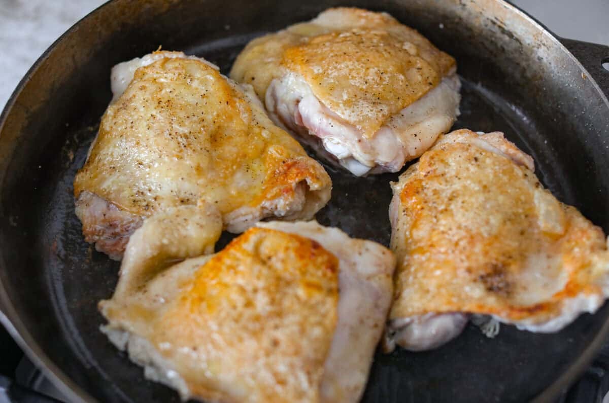 Chicken thighs browning in a skillet. 