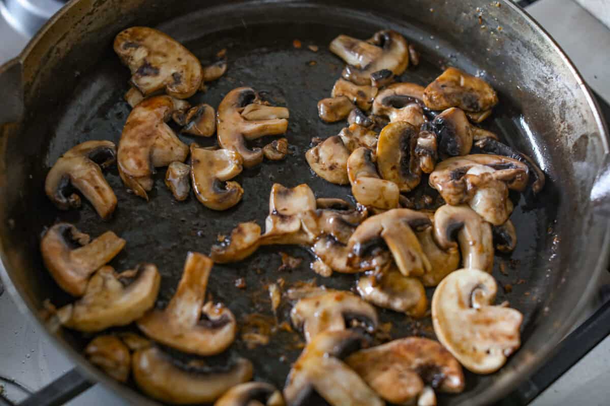 Mushrooms cooking in olive oil in a skillet.