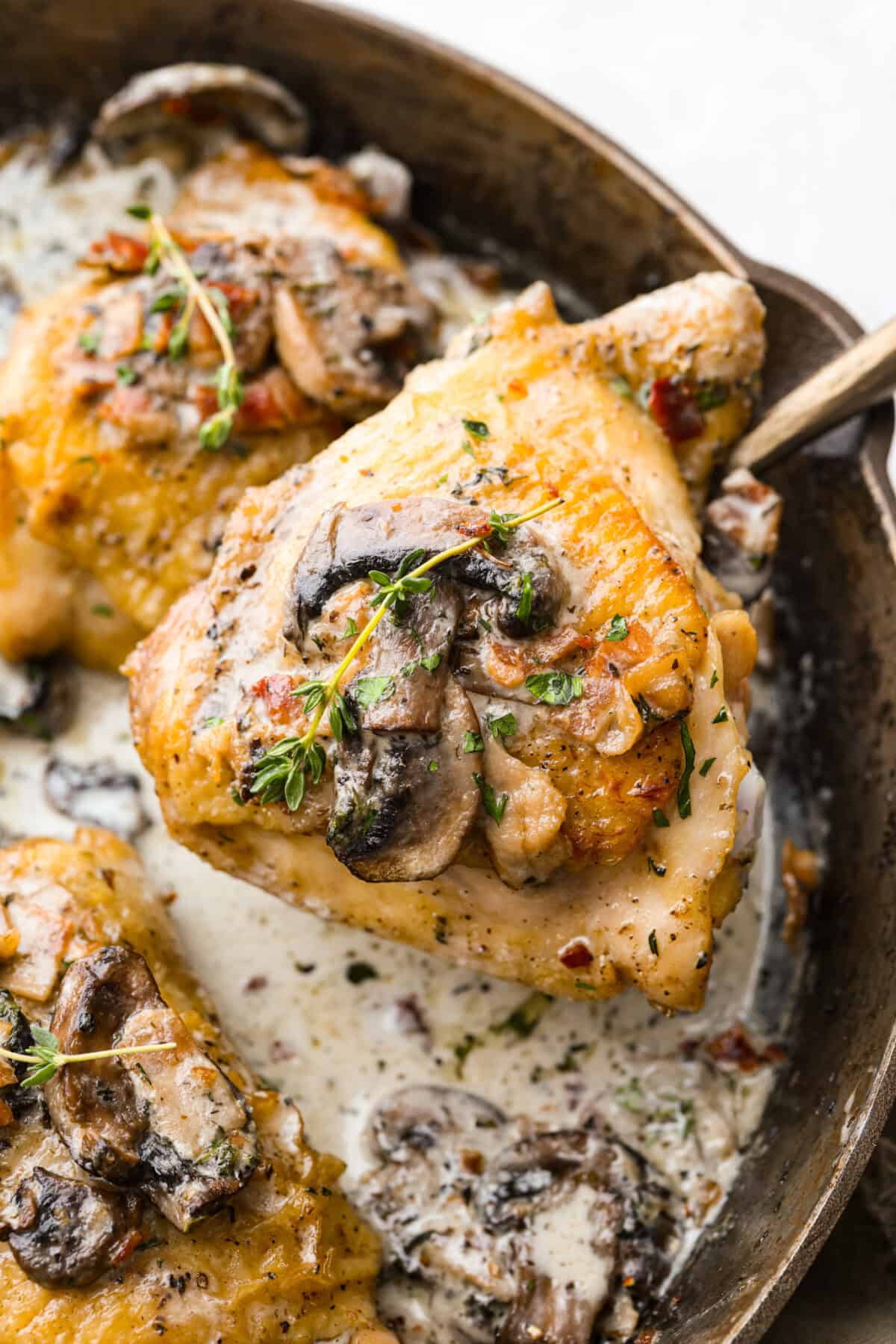 Someone lifting out a bacon mushroom thyme chicken thigh out of the skillet. 