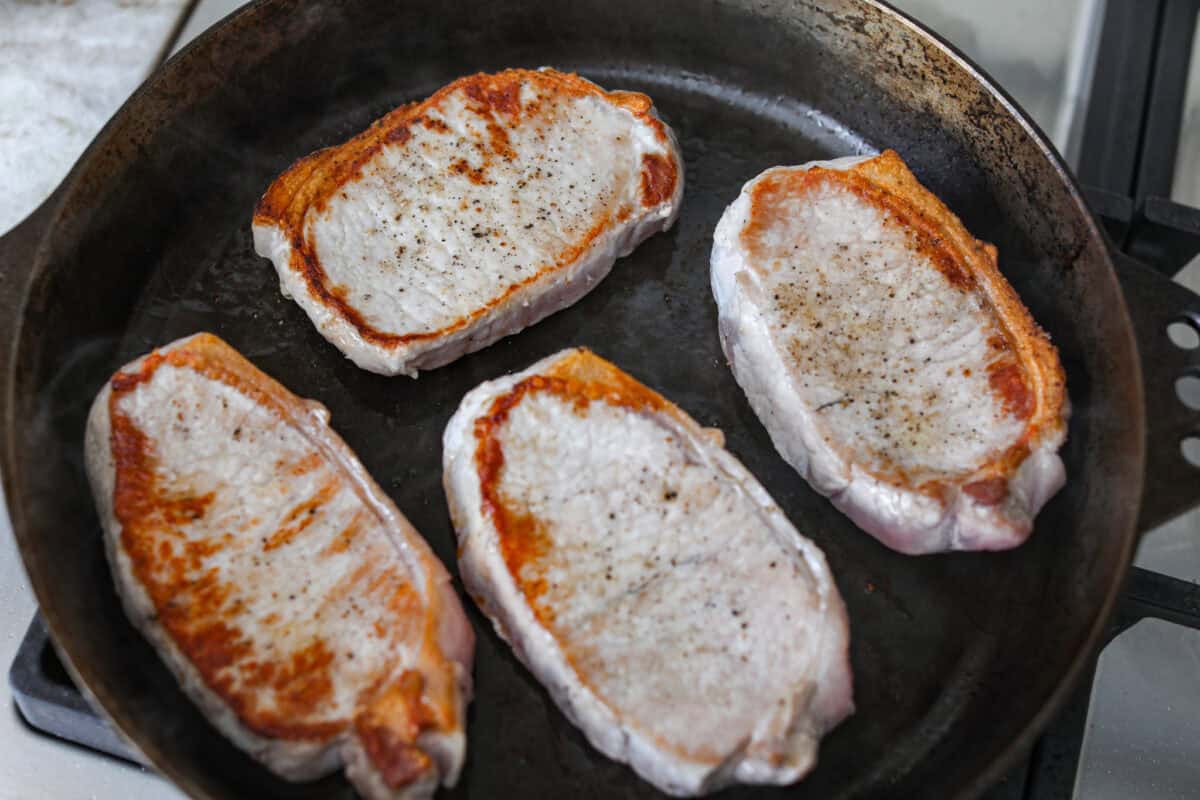 Seasoned pork chops being seared in a skillet. 