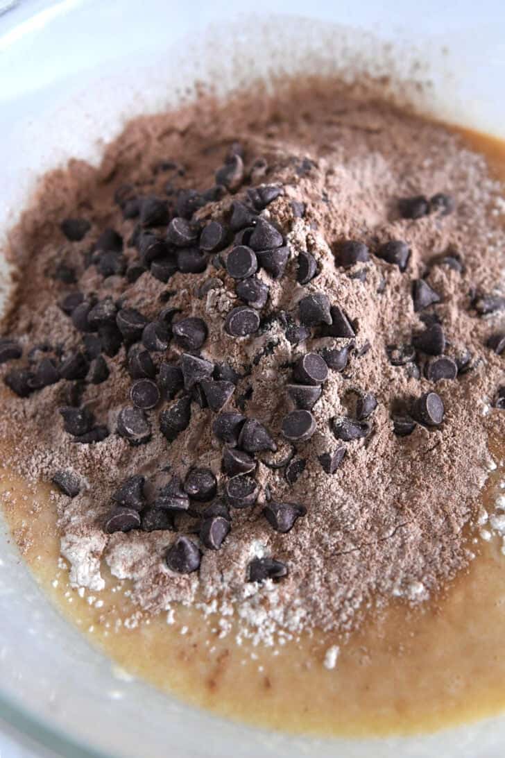 Glass bowl with banana bread batter, cocoa powder, chocolate chips.