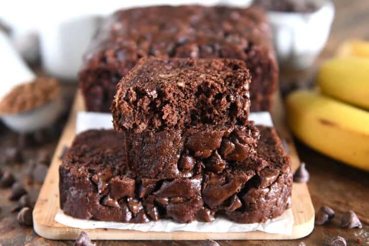 Two slices of chocolate banana bread stacked on parchment paper and wood cutting board.