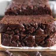 Two slices of chocolate banana bread stacked on parchment paper and wood cutting board.