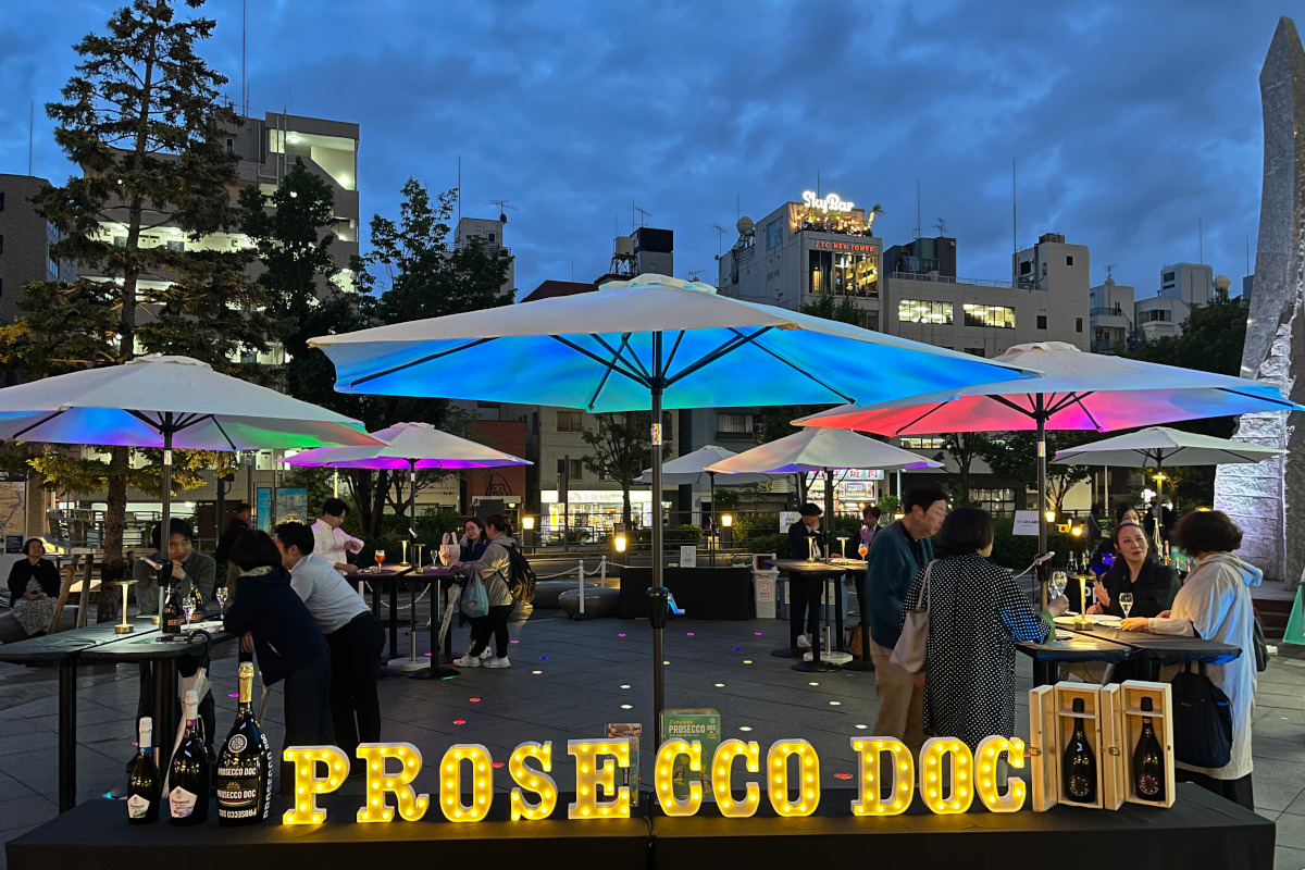 Outdoor Prosecco DOC garden event in Tokyo Skytree Town. People drinking Prosecco under colorful umbrellas at dusk.