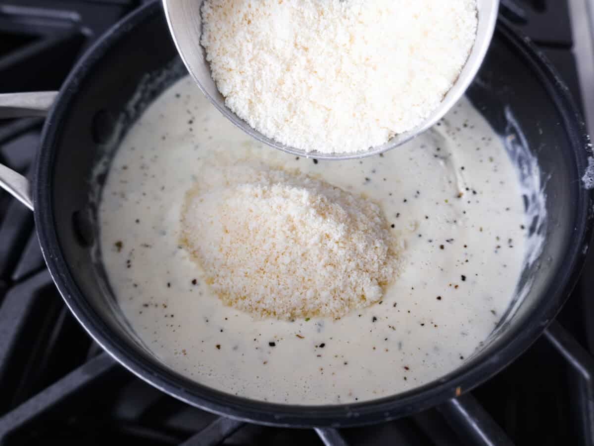 Parmesan cheese being added to the cream and seasoning mixture. 