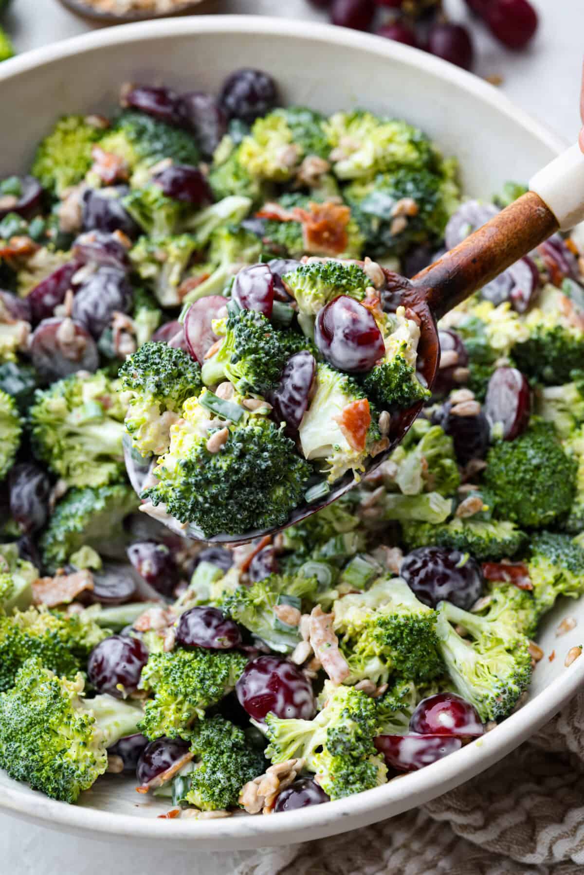 Someone lifting out a scoop of broccoli grape salad from the large serving bowl.