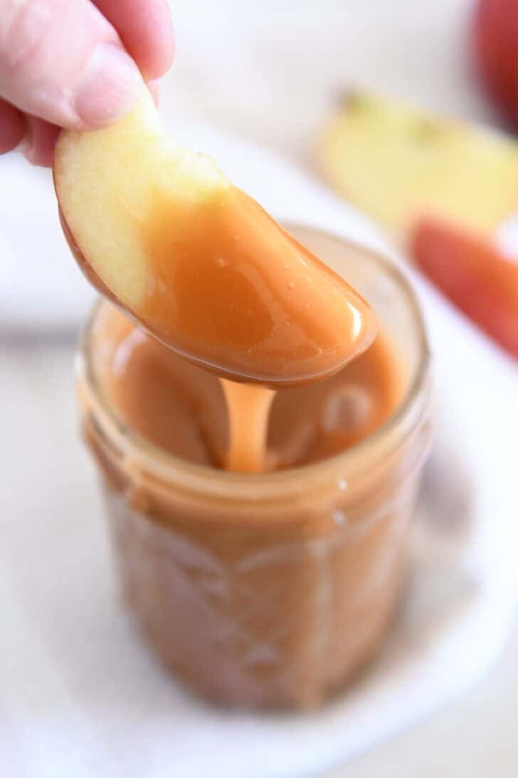 Dipping apple slice into jar of caramel sauce.