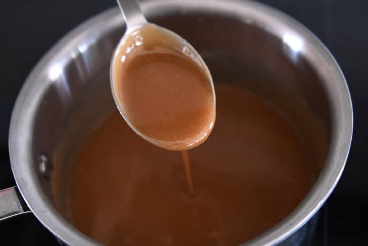 Spoon drizzling hot caramel sauce into saucepan.