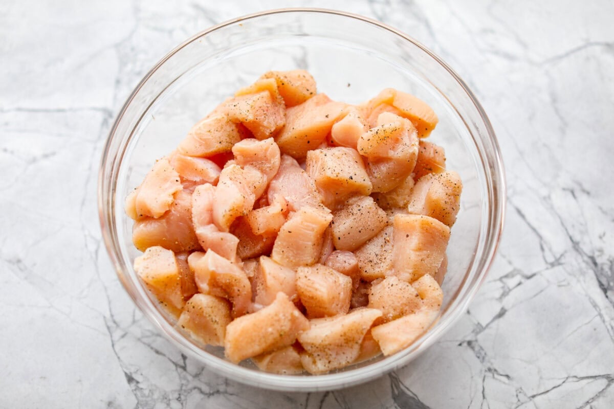 Chicken breast cut up and seasoned in a bowl. 