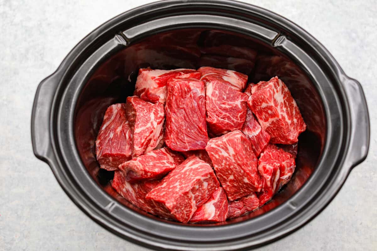 Beef added to a slow cooker. 
