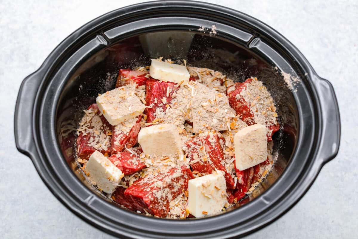 Onion soup mix and butter added to the beef in the slow cooker.